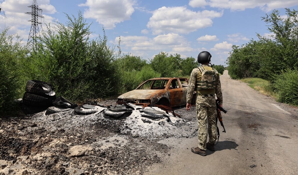 Een Oekraïense soldaat staat bij de overblijfselen van een uitgebrande auto.  (beeld Daphne Wesdorp)