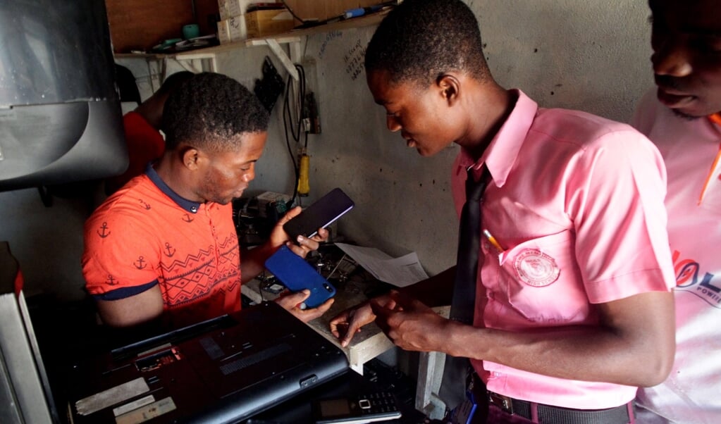 Een klant overlegt met Hassan Lamie (links), die in de Liberiaanse hoofdstad Monrovia mobiele telefoons repareert. Lamie illustreert dat jonge Afrikanen steeds vaker goed opgeleid zijn.  (beeld epa / Ahmed Jallanzo)