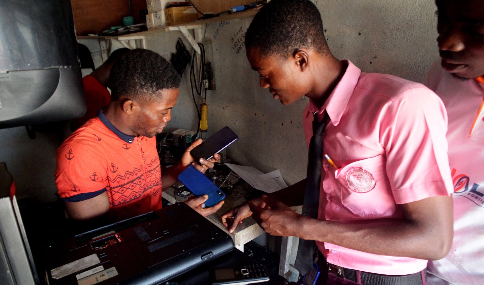 Een klant overlegt met Hassan Lamie (links), die in de Liberiaanse hoofdstad Monrovia mobiele telefoons repareert. Lamie illustreert dat jonge Afrikanen steeds vaker goed opgeleid zijn.