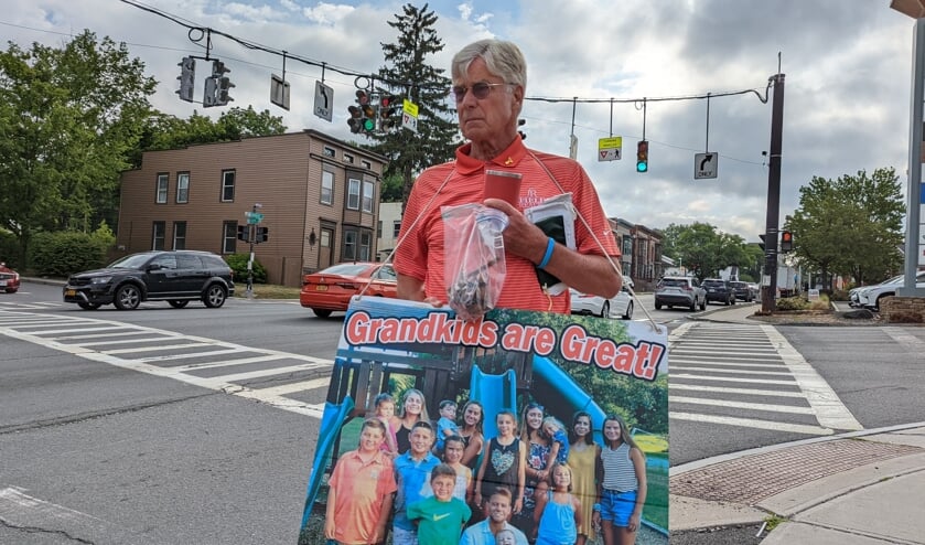 Rick Field draagt een bord met daarop de tekst 'Kleinkinderen zijn geweldig!' en een foto van alle zestien.