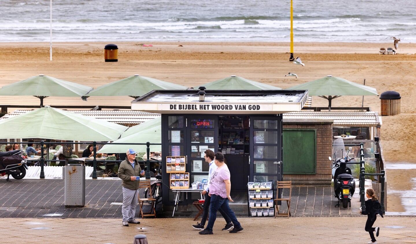 Op zondag bemant Henk Ligtvoet (met petje) regelmatig de Bijbelkiosk op de Boulevard van Scheveningen. Deze zondag is regenachtig; tussen de buien door spreekt Henk de voorbijgangers aan.