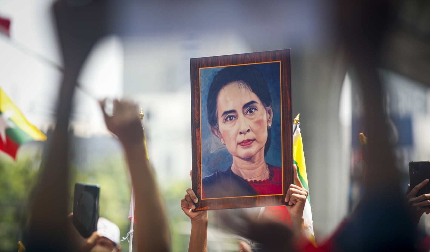 Aanhangers houden nationale vlaggen van Myanmair en een grote afbeelding van het Myanmarese democratie-icoon Aung San Suu Kyi vast. 
