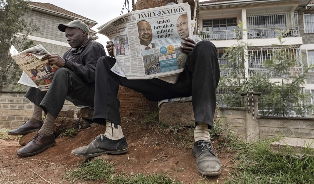 Twee Keniaanse mannen lezen langs de kant van de weg het laatste nieuws over de verkiezingen.  (beeld afp / Tony Karumba)