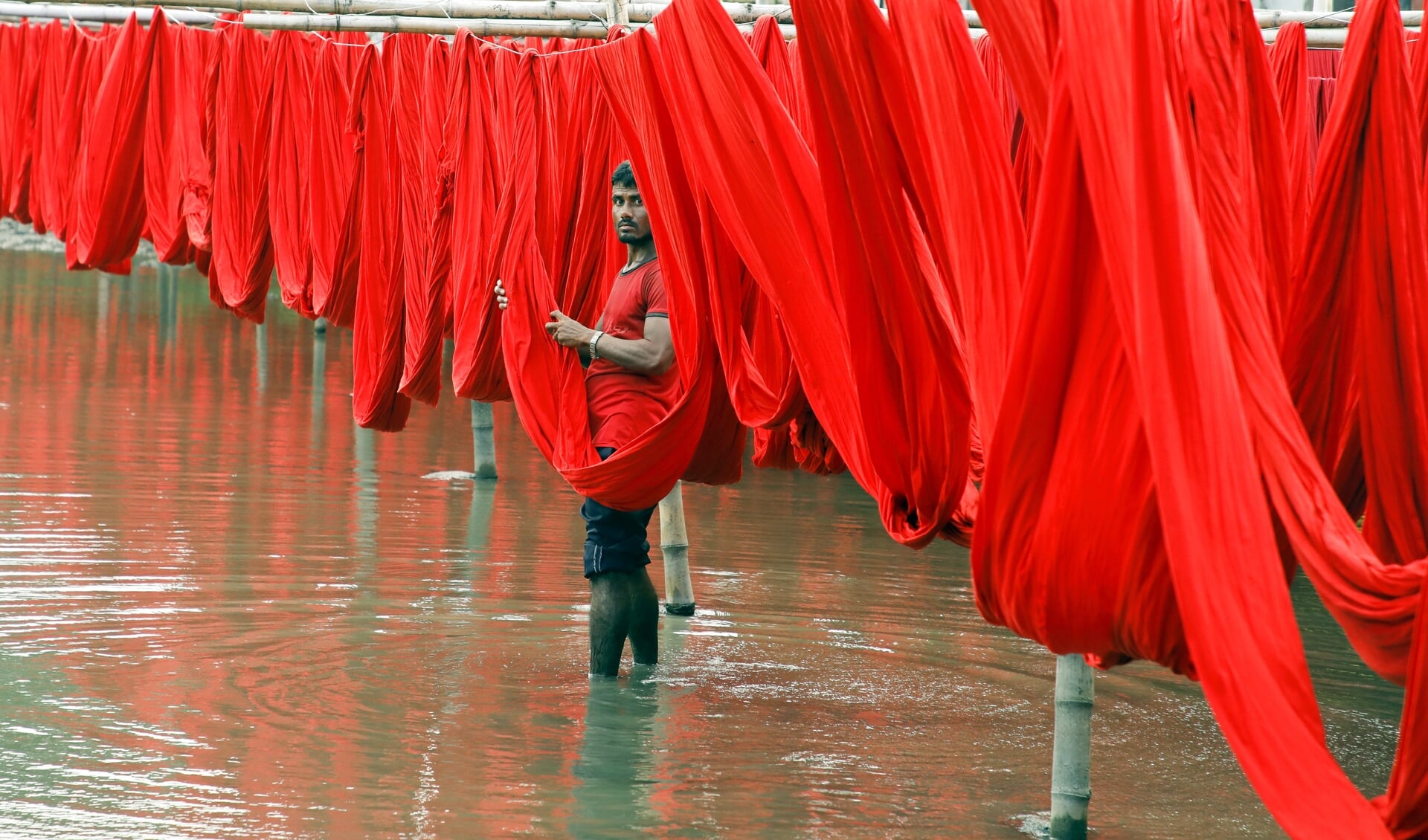 Een medewerker in een fabriek in Narayangani, Bangaladesh, droogt stoffen nadat kleurstof is toegevoegd. Bangladesh is een van de grootste exporteurs van kleding ter wereld. Veel westerse landen laten er hun kleding maken.