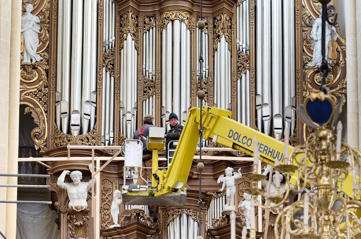Orgelbouwers sturen behoedzaam de hoogwerker langs de kroonluchter. Het dreigt beschadigd te raken bij de renovatie van de Kamper Bovenkerk. 