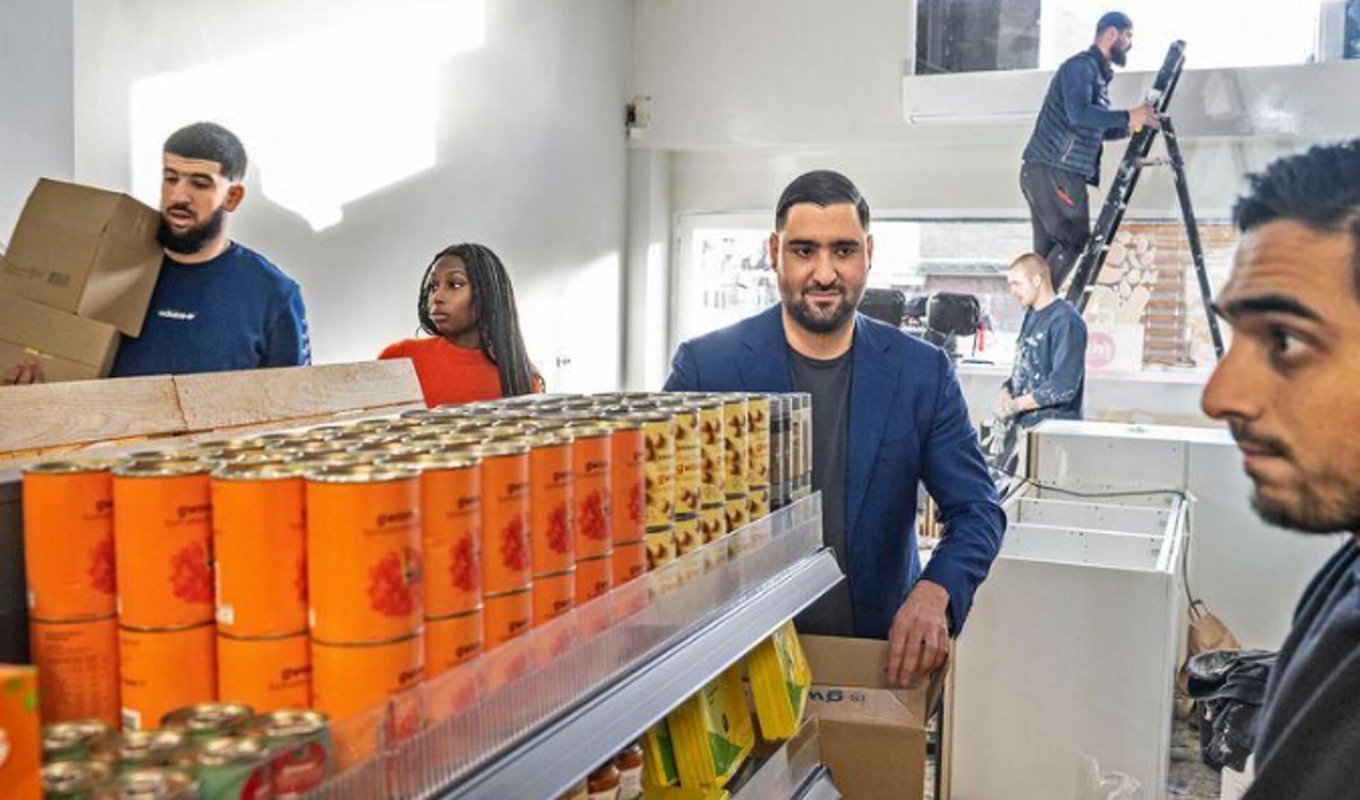 Abdelhamid Idrissi, midden, helpt met het vullen van de vakken van zijn gratis supermarkt.