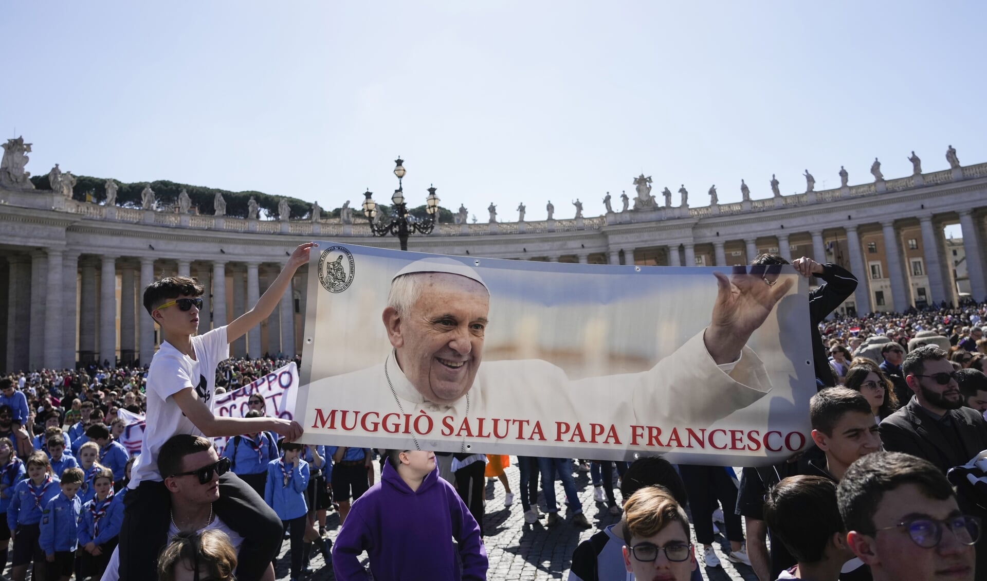 Gelovige op het Sint Pieterplein in Vaticaanstad houden een groeten de paus met een spandoek.