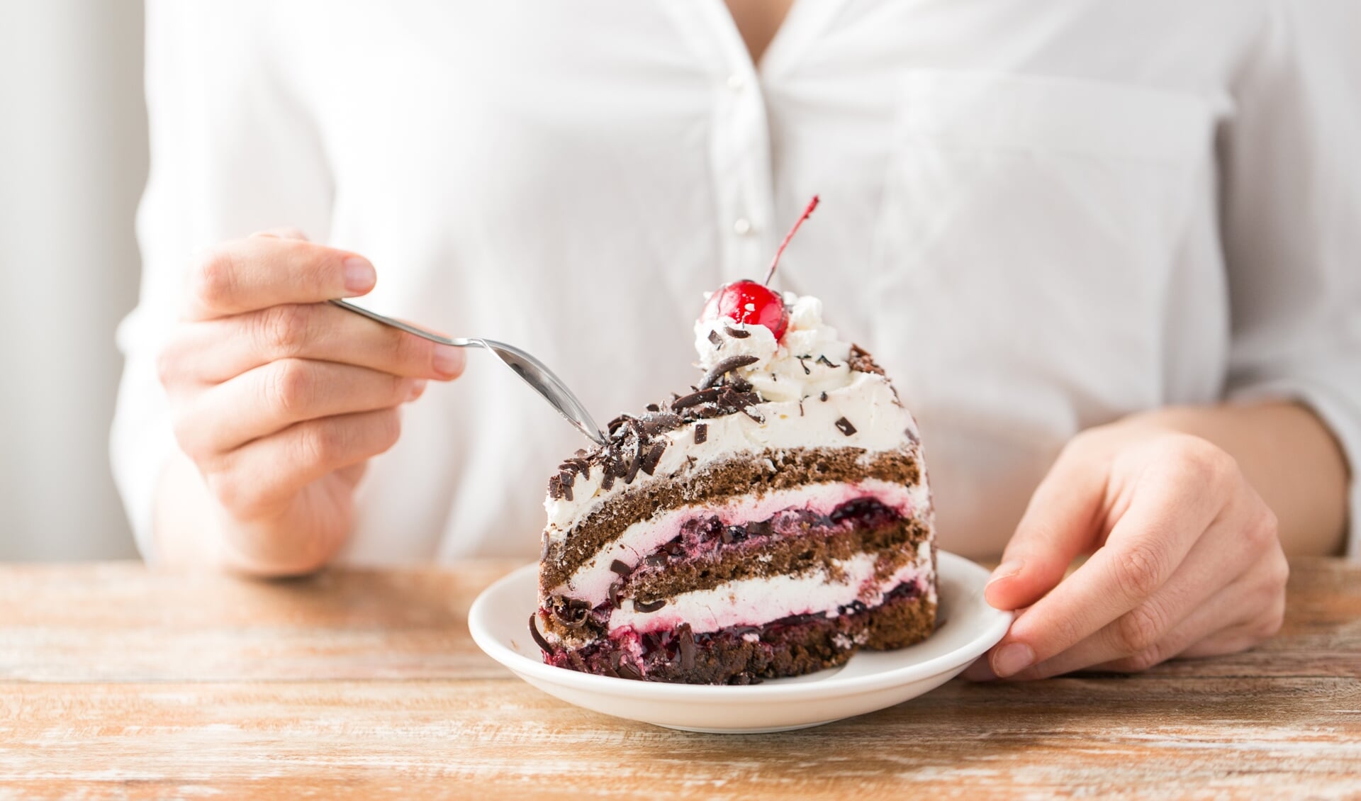 food, dessert and pastry concept - close up of woman eating piece of chocolate layer cake with maraschino cherry