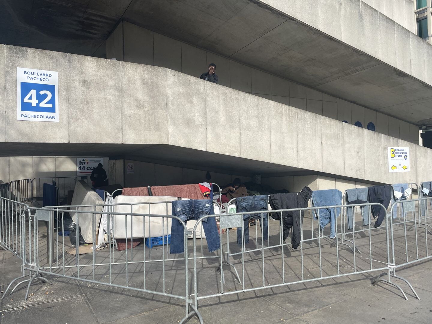 Asielzoekers verblijven onder een betonnen oprit naast het kantoor van de vreemdelingendienst.