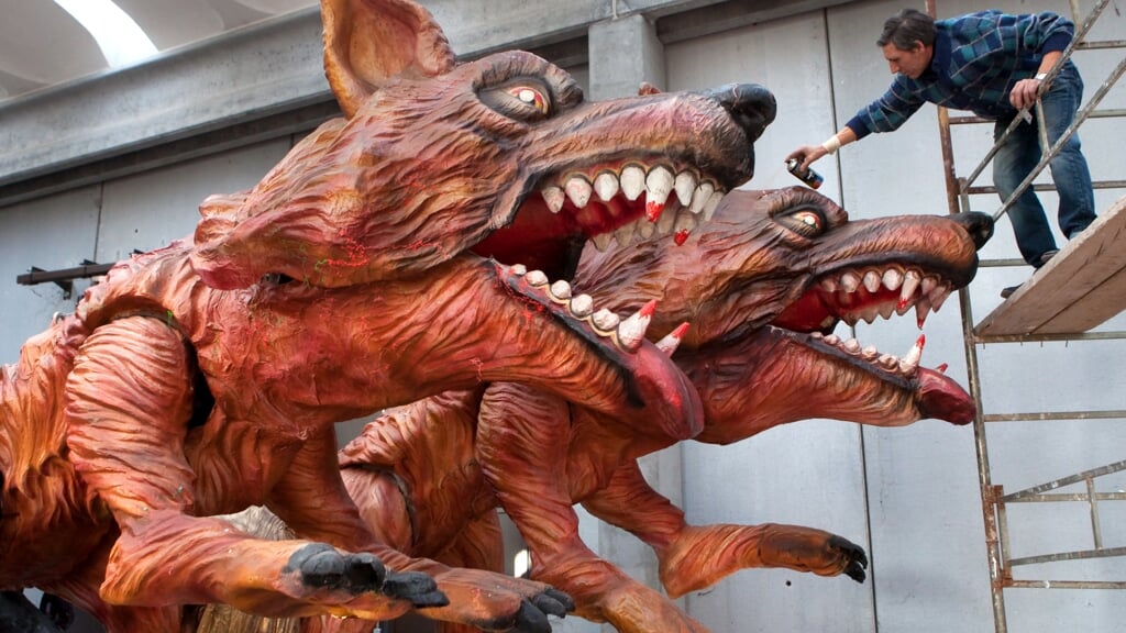 Een man legt de laatste hand aan een paar reusachtige wolven op een paradekar voor de carnavalsoptocht.
