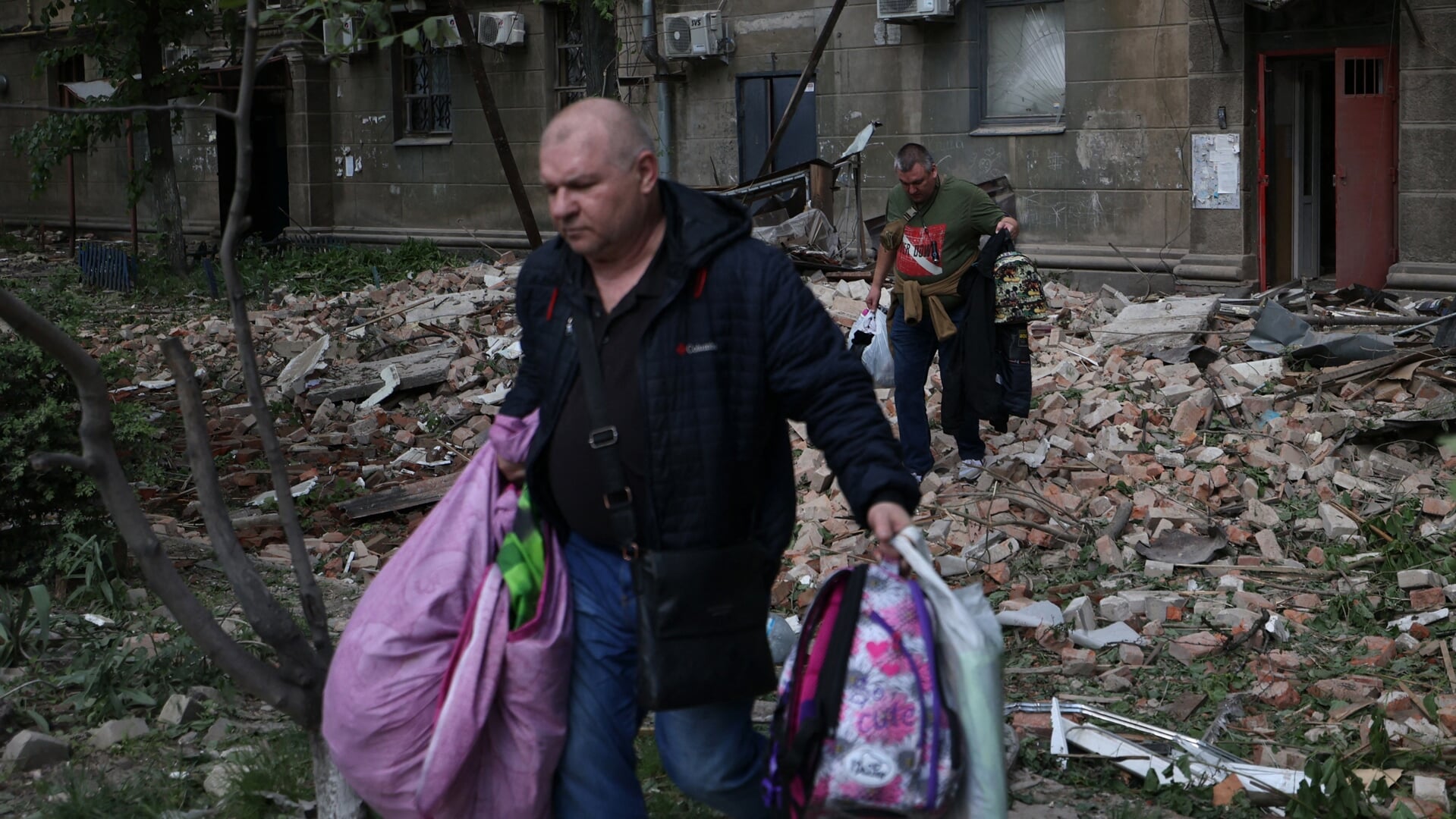 Bewoners vluchten met wat eigendommen uit hun huis in Dnipro dat beschadigd raakte bij een Russische raketaanval. 