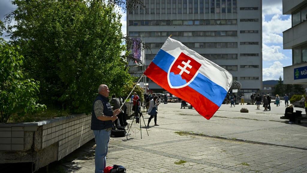 Met een Slowaakse vlag in zijn handen staat een man bij het ziekenhuis waar de neergeschoten Robert Fico wordt verpleegd. De man met de vla bidt voor het herstel van de premier.  