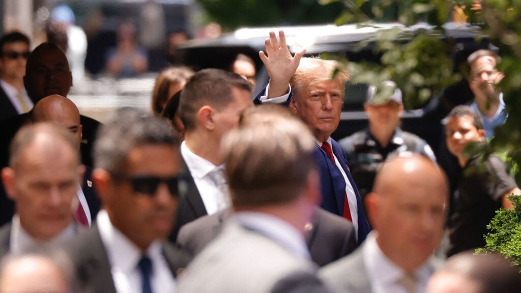 Trump zwaait - omringd door beveiligers van de Secret Service - naar zijn aanhangers bij het verlaten van de Trump Towers. Als hij celstraf krijgt, moet die dienst hem ook in de gevangenis 24 uur per dag beveiligen.