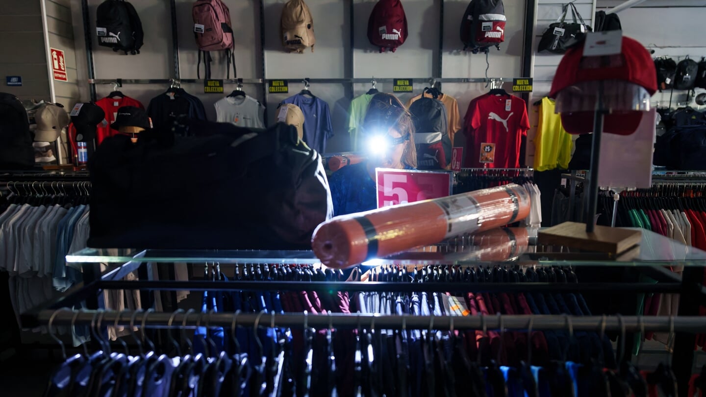 Een medewerker van een sportwinkel in het Spaanse Burgos omzeilt de stroomstoring door een mijnlamp op haar hoofd te gebruiken.