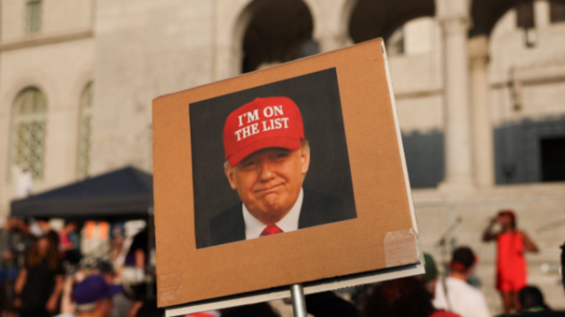 Een demonstrant houdt een bord omhoog met een bewerkte foto van Trump met de tekst 'ik sta op de lijst', wat een verwijzing naar de 'Epstein lijst' van Jeffrey Epstein. Terwijl deze kwestie vol in de belangstelling staat, krijgt Project 2025 nauwelijks nog aandacht.