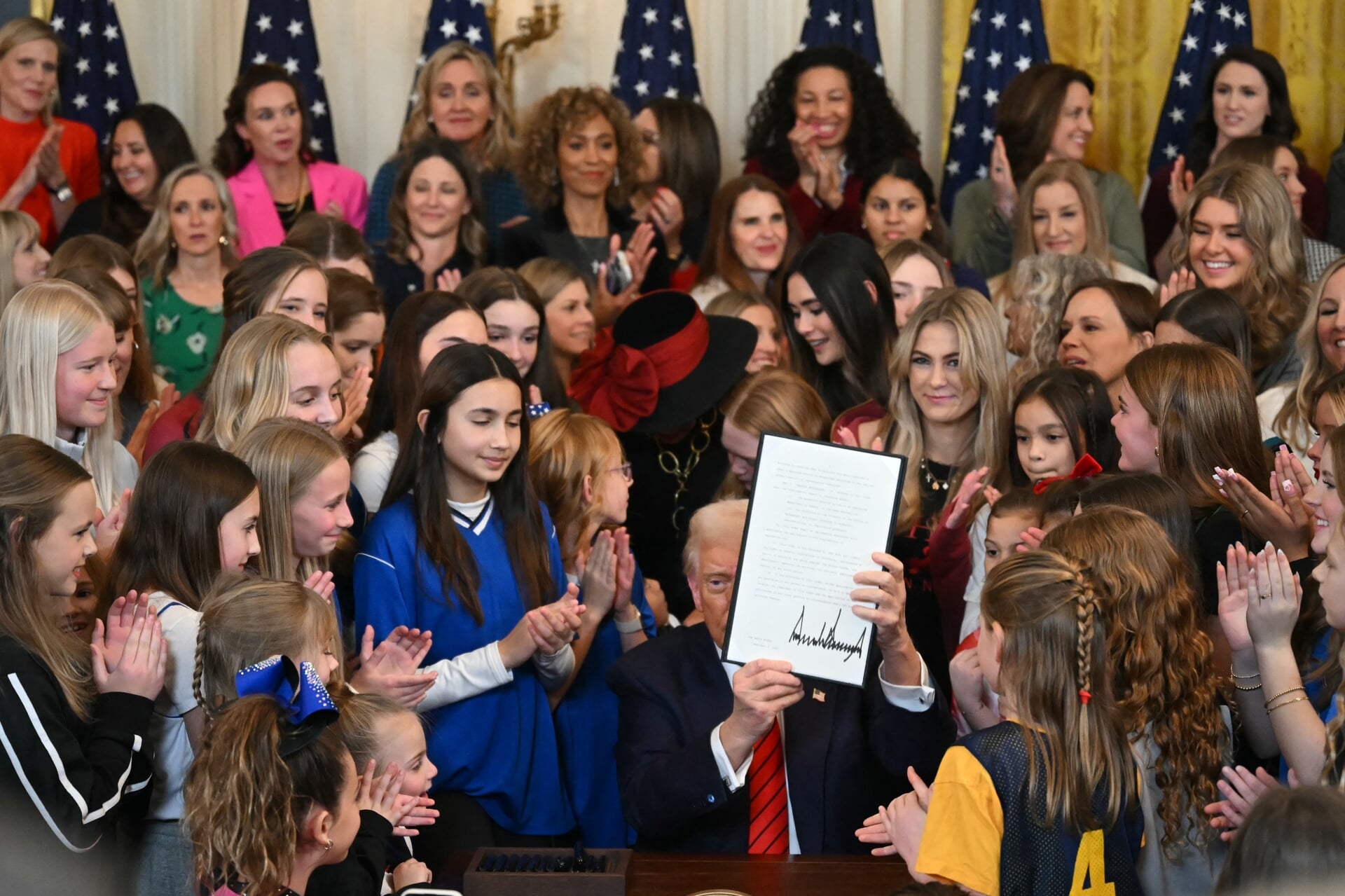 Omringd door applaudisserende vrouwen en meisjes toont Donald Trump twee weken na zijn aantreden als president het decreet waarmee hij alle trans personen belooft te verbannen uit vrouwencompetities.