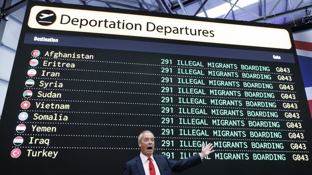 Reform UK-leider Nigel Farage wijst dinsdag naar een zelfgemaakt vertrekbord met verzonnen aantallen migranten.