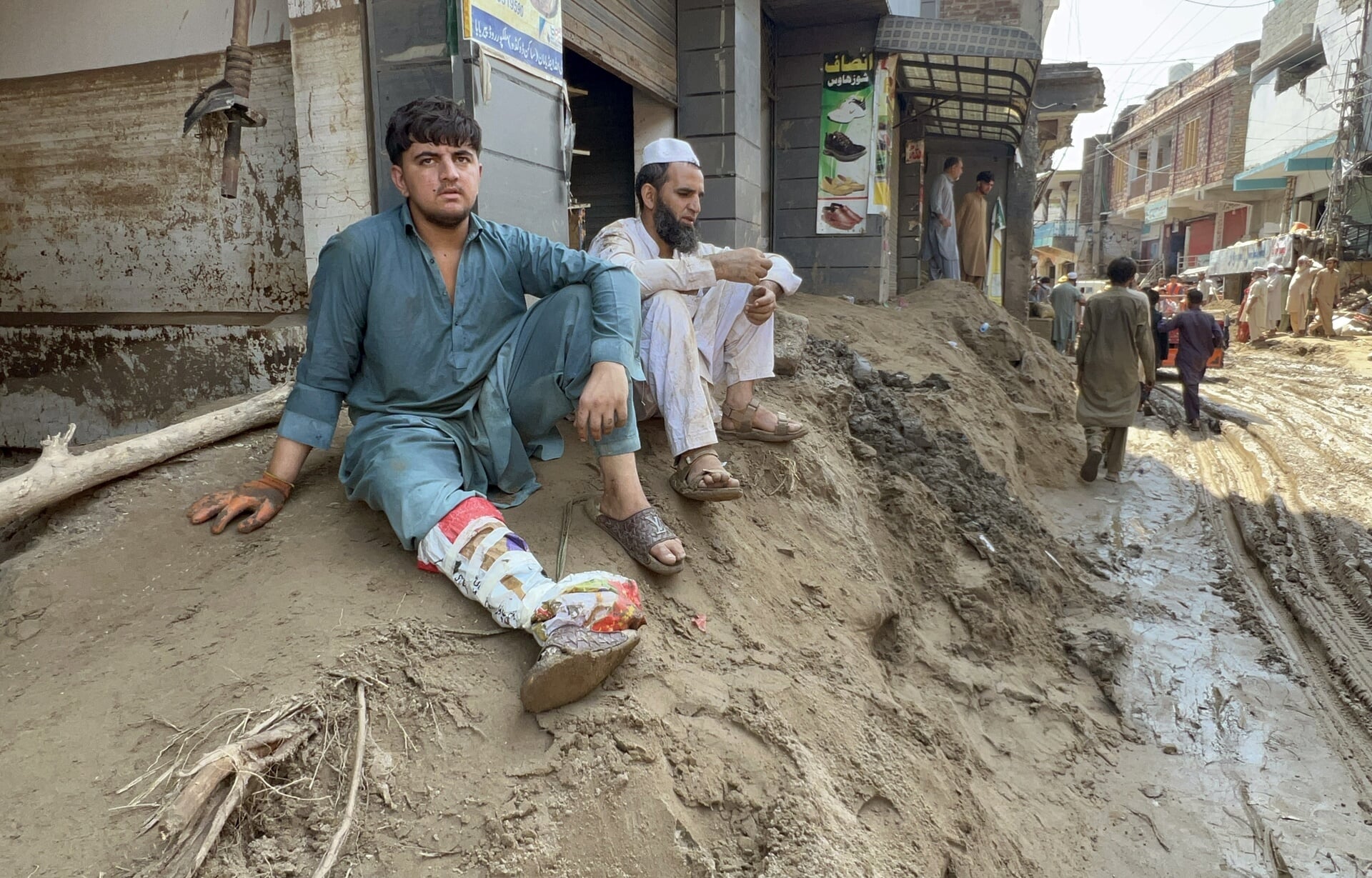 Winkeliers scheppen de modder uit hun zaak in Swabi, Pakistan. Daar kwamen woensdag minstens 17 mensen om.