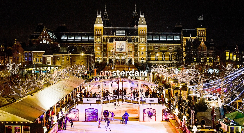 Op het Museumplein in Amsterdam is vrijdagavond een kerstmarkt geopend onder de naam Christmas Village. De markt en de tijdelijke kunstijsbaan zijn sfeervol verlicht, maar het zal niet meevallen er een winters gevoel bij te krijgen (anp / Remko de Waal)