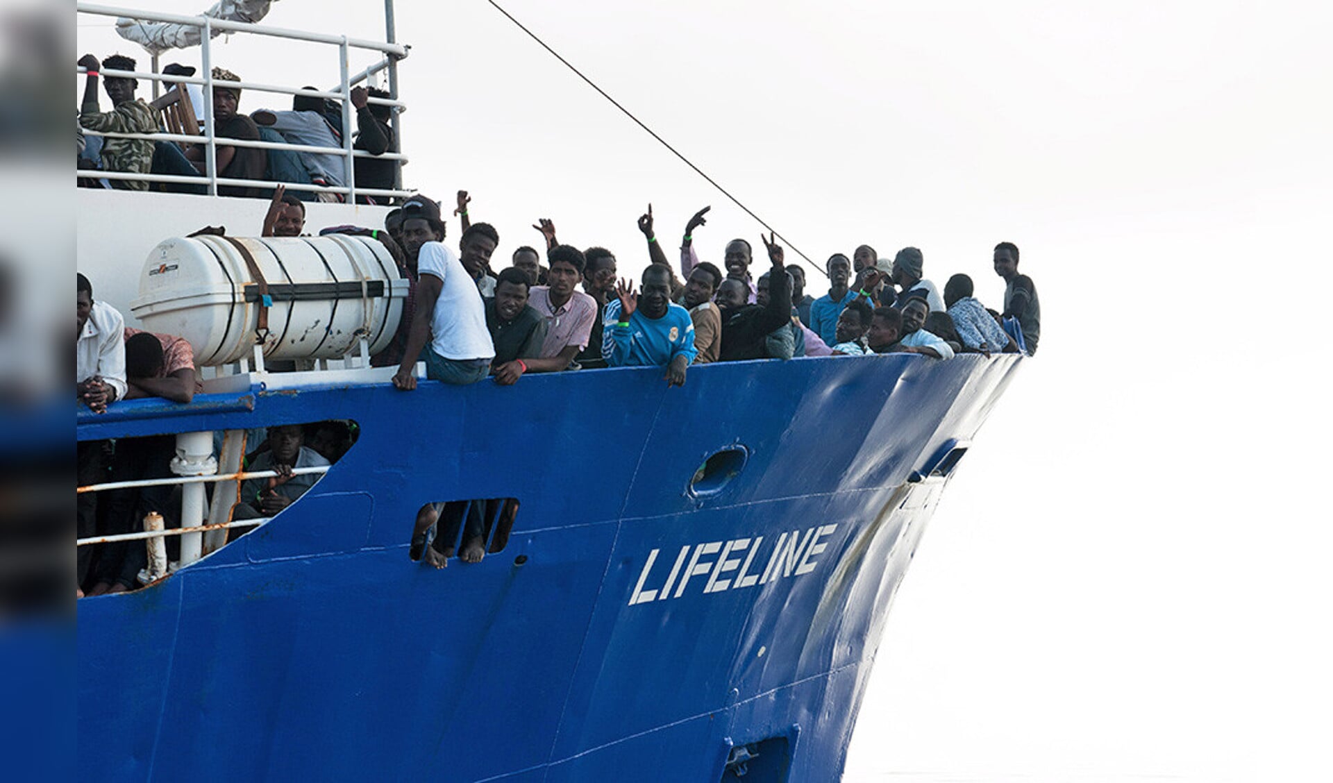 Op het voordek van de Lifeline staan migranten die uit de internationale wateren van de Middellandse Zee zijn gered.