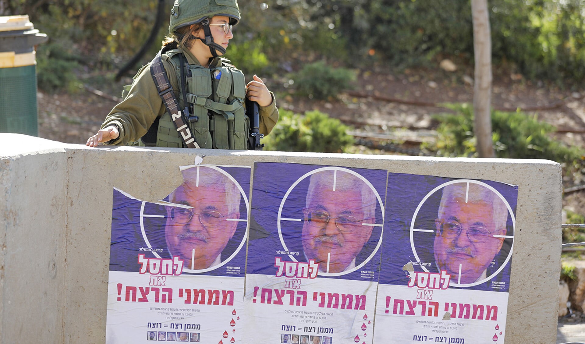 Een Israëlische soldaat naast posters met een foto van president Mahmoud Abbas van de Palestijnse Autoriteit.