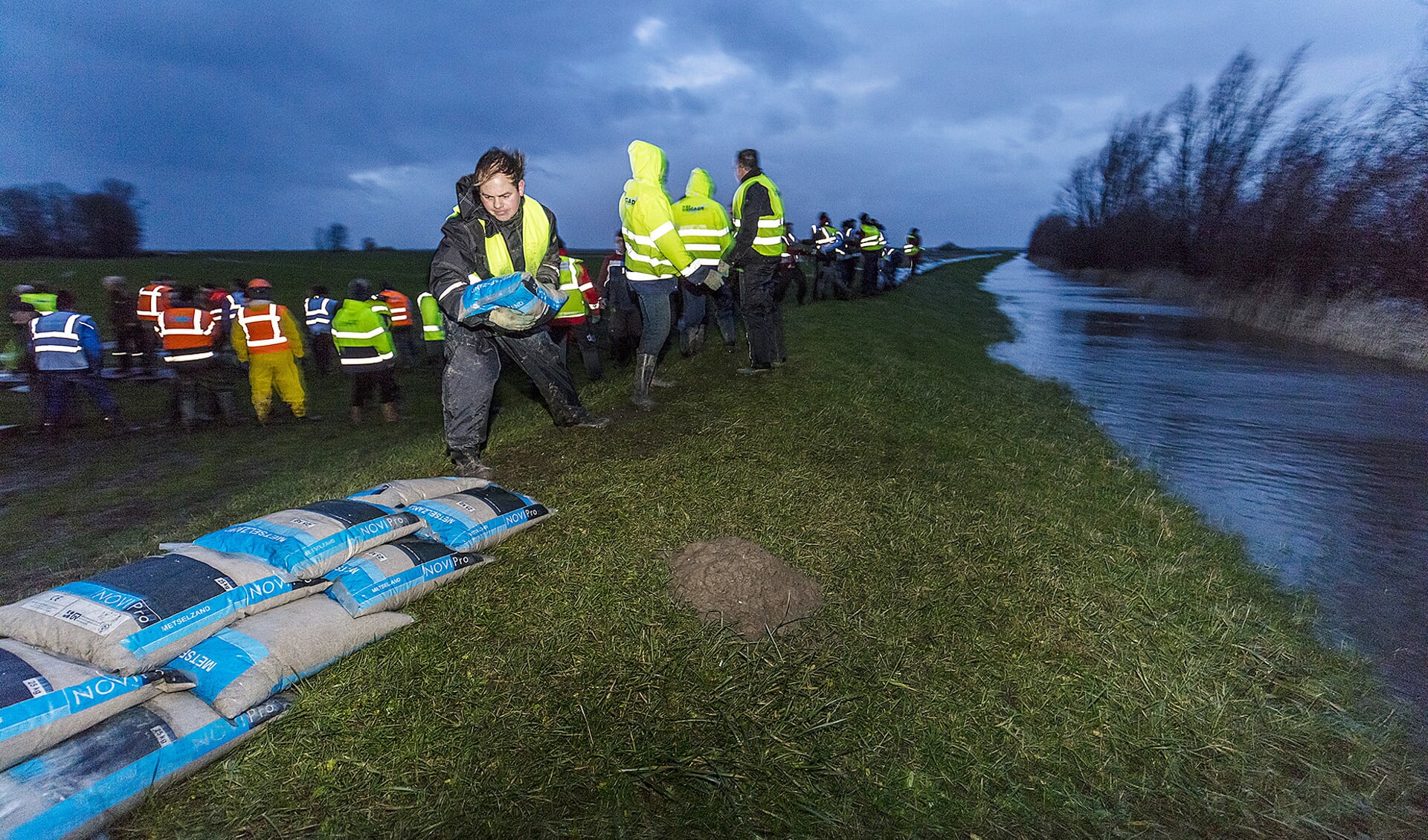Vrijwilligers stapelen tegen het hoge water zandzakken op in de polder Mandjeswaard bij Kampen.