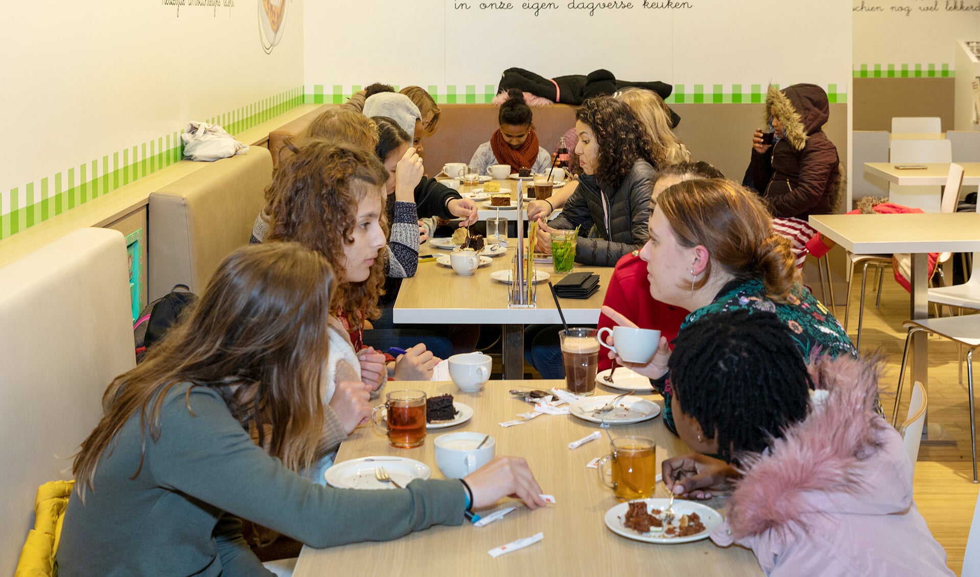 Oprichtster Marije van den Berg (rechts voor) in gesprek met tieners bij de wekelijkse meidenclub in Ede. Naast haar (roze jas) zit de Eritrese Bana.