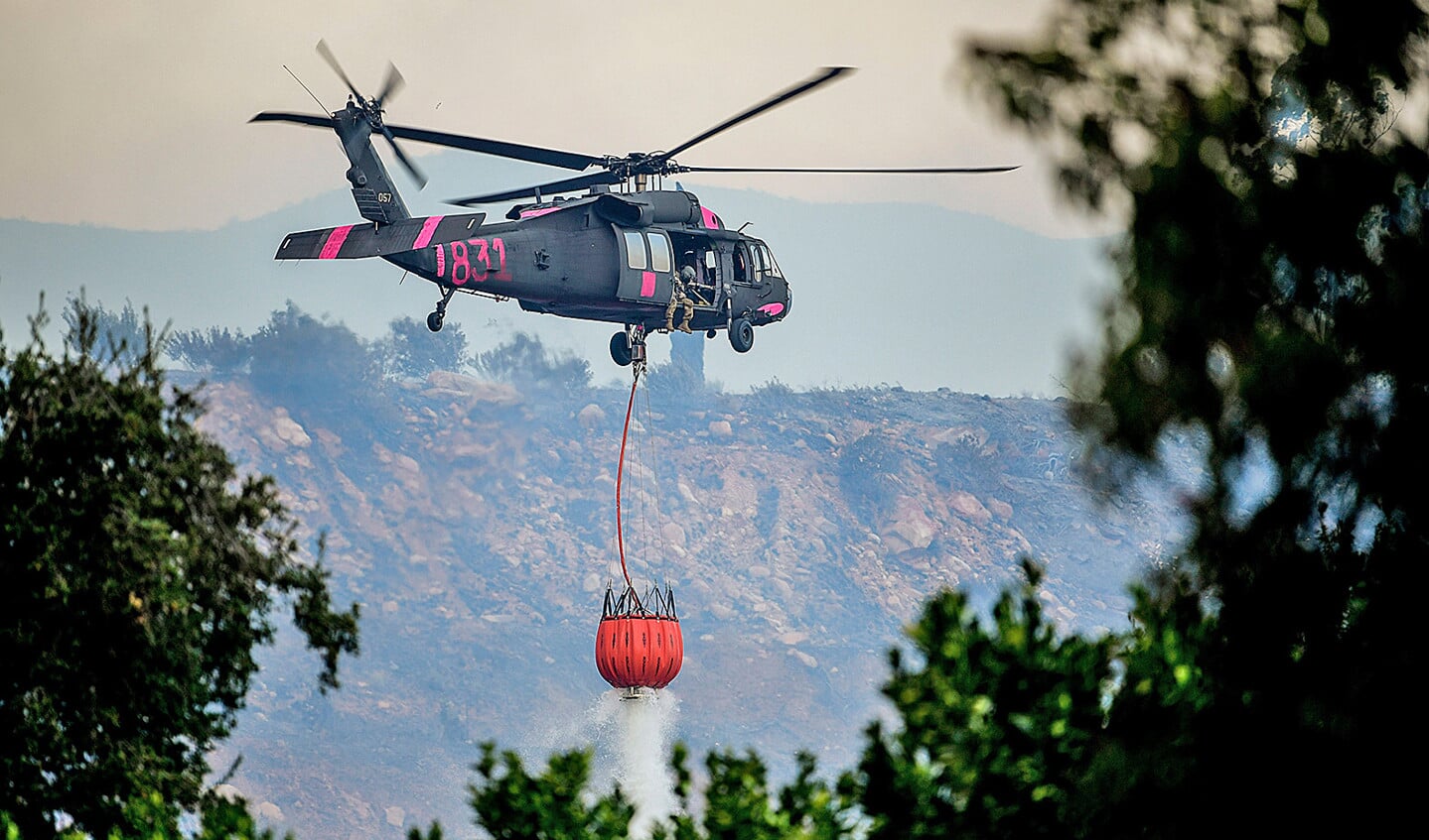 Bij de bestrijding van de natuurbranden in Californië wordt ook gebruikgemaakt van militaire helikopters. Die voeren bakken met water aan, dat boven de vuurzee wordt uitgestort.