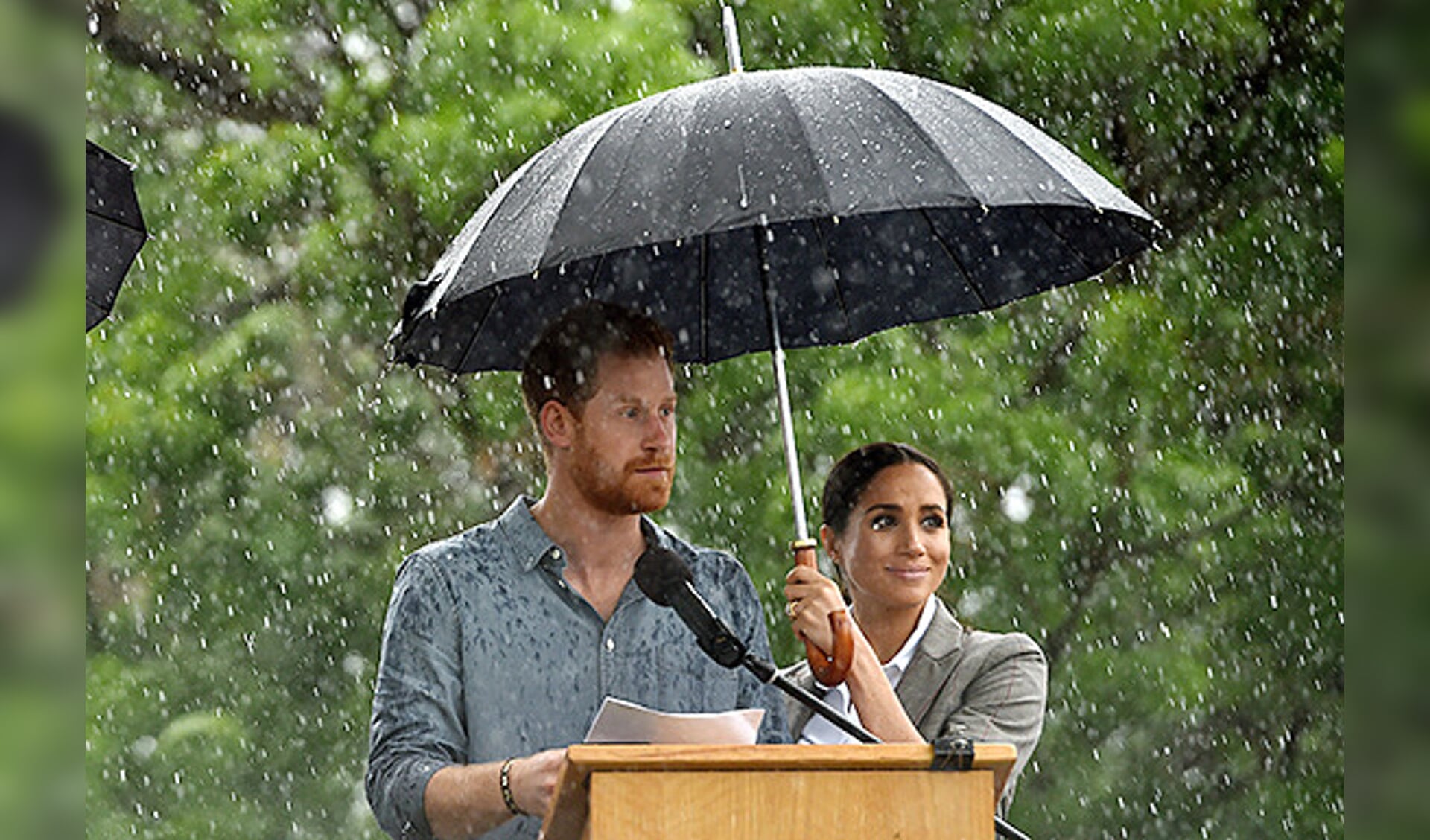 Prins Harry spreekt de in het Victoria Park verzamelde menigte toe vanonder een paraplu.