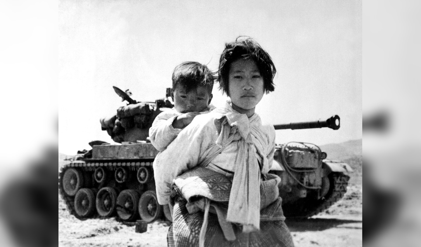 Met haar broertje op de rug sjokt een Koreaans meisje langs een vastgelopen M-26 tank. Deze foto werd genomen bij de Koreaanse plaats Haengju op 9 juni 1951.