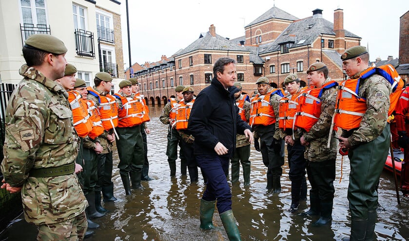 David Cameron stapt met laarzen door het water in het graafschap Yorkshire. Hij bezocht het gebied maandag om de soldaten, die helpen mensen te evacueren, een hart onder de riem te steken. (ap / Darren Staples)
