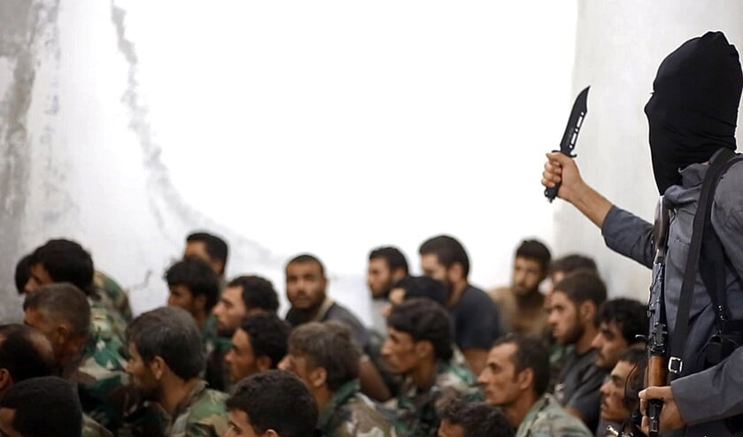 Een strijder van ISIS, gewapend met een mes en een automatisch wapen, bewaakt Syrische soldaten die worden gebruikt als menselijk schild. (ap)