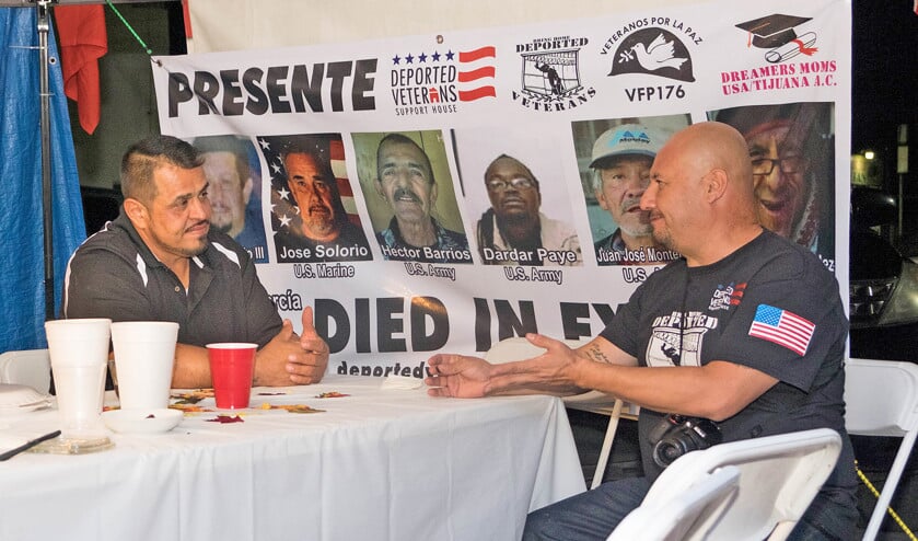 Hector Barajas (rechts) en Enrique Salas (47) na een gezamenlijk diner buiten ‘De Bunker’. Achter hen hangt een spandoek met Amerikaanse veteranen die in Tijuana zijn overleden. (Eline van Nes)