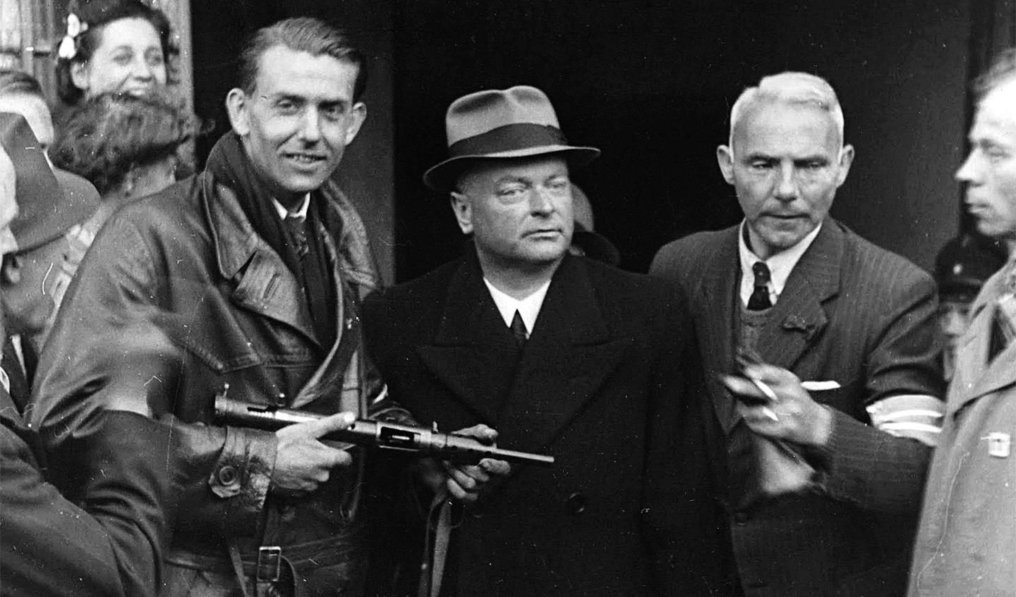 De arrestatie van NSB-leider Anton Mussert. Links een lid van de Binnenlandse Strijdkrachten, rechts twee topfunctionarissen van de Haagse politie, J.G. Krabbendam en G.W. Valken.