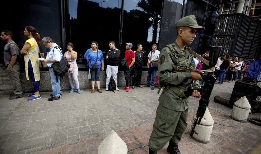 Een Venezolaanse soldaat bewaakt de straat, terwijl mensen in de rij staan om hun waardeloos geworden biljetten van 100 bolivar in te leveren. Volgens persbureau AP verrijkt het leger zich schaamteloos in het Zuid-Amerikaanse land.  (ap / Fernando Llano)