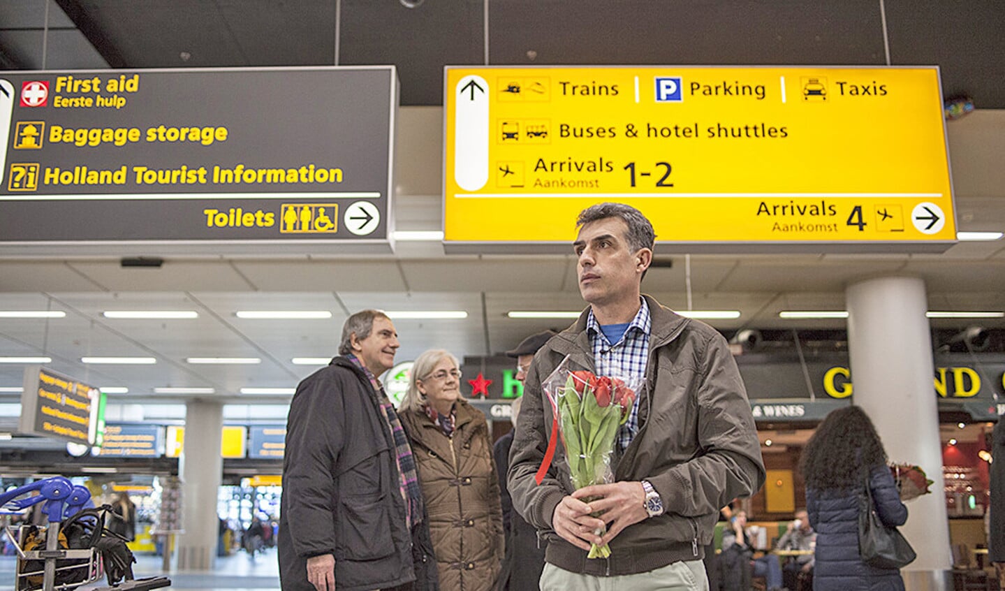 Stijf van de zenuwen wacht Syros in de aankomsthal op Schiphol op zijn gezin. Hij heeft hen bijna vijf jaar niet gezien.