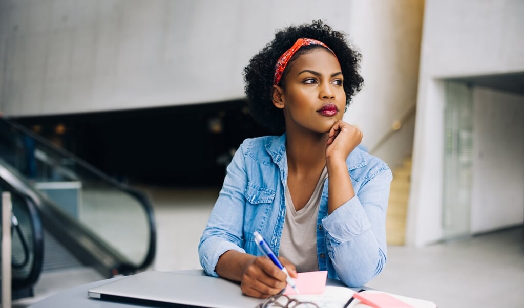 Focused young African female entrepreneur deep in thought while working at a table in a modern office building lobby ( beeld Getty Images/iStockphoto)