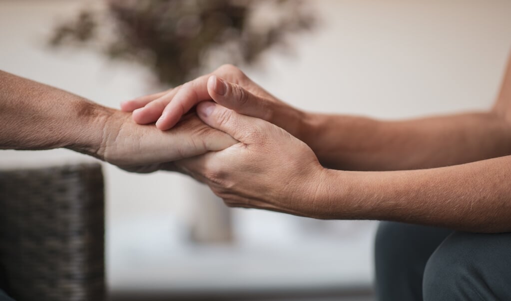 Two people are sitting down, and one person is holding and caressing another hand. The picture is a close-up of the hands. (beeld istock)