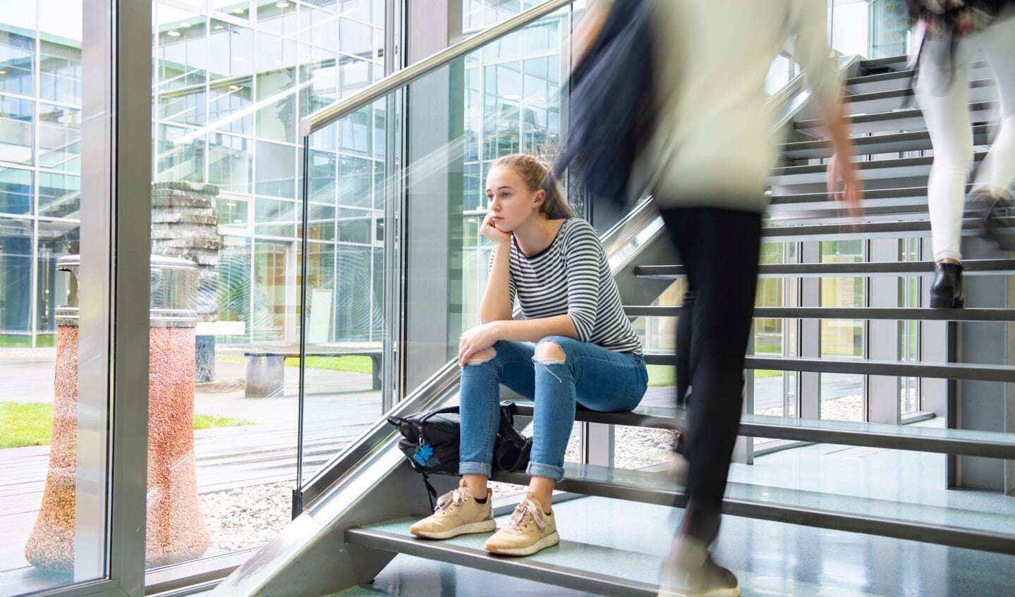 High school students walking on stairs between lessons in college building,sad schoolgirl sitting alone on staircase