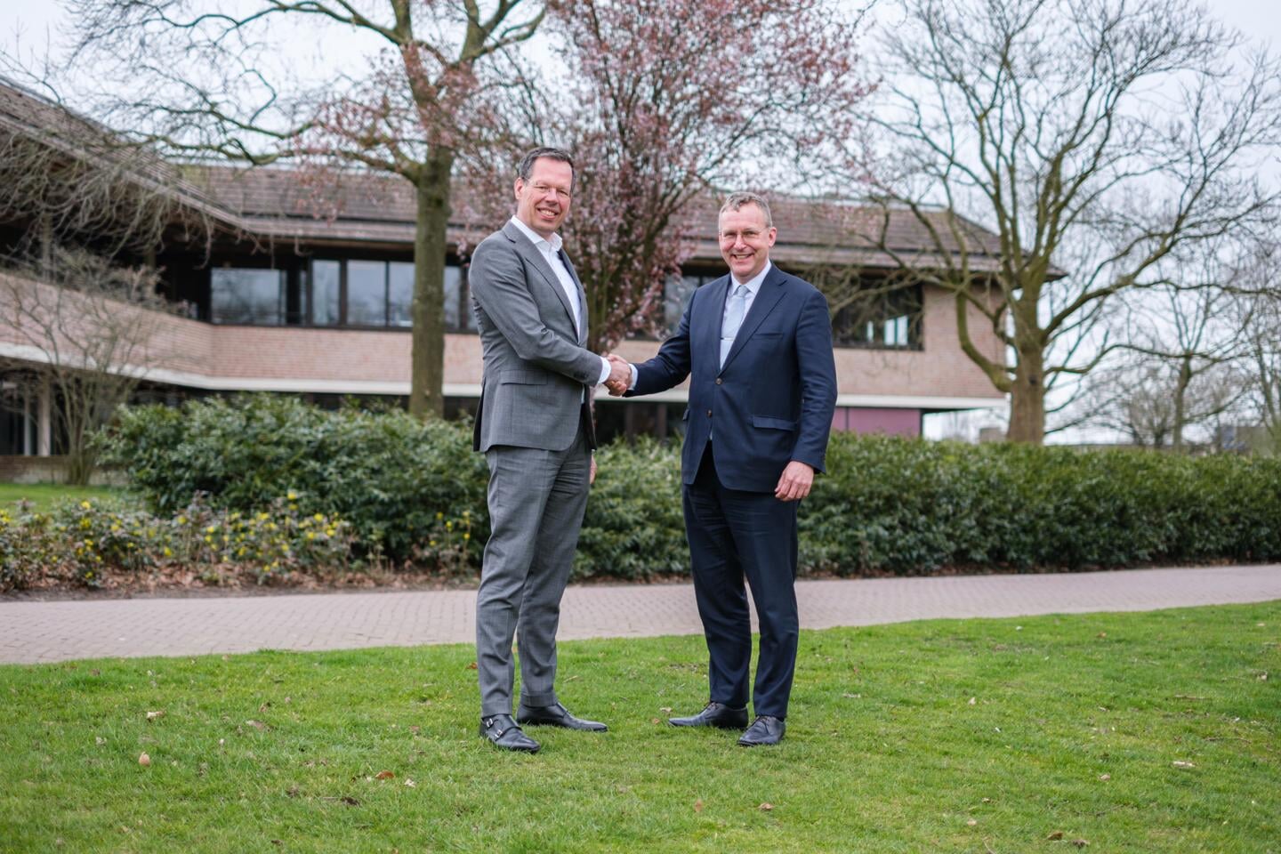 Roger Beuting, algemeen directeur van ROVA, (links) en wethouder Bart Jaspers Faijer (rechts) schudden elkaar de hand voor het gemeentehuis. 