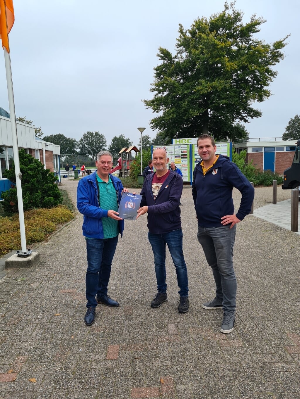 De bestuursleden Marthijn Binnenmars en Jan Bosch  bieden de gids aan wethouder sportzaken van de gemeente Twenterand, Mark Paters.