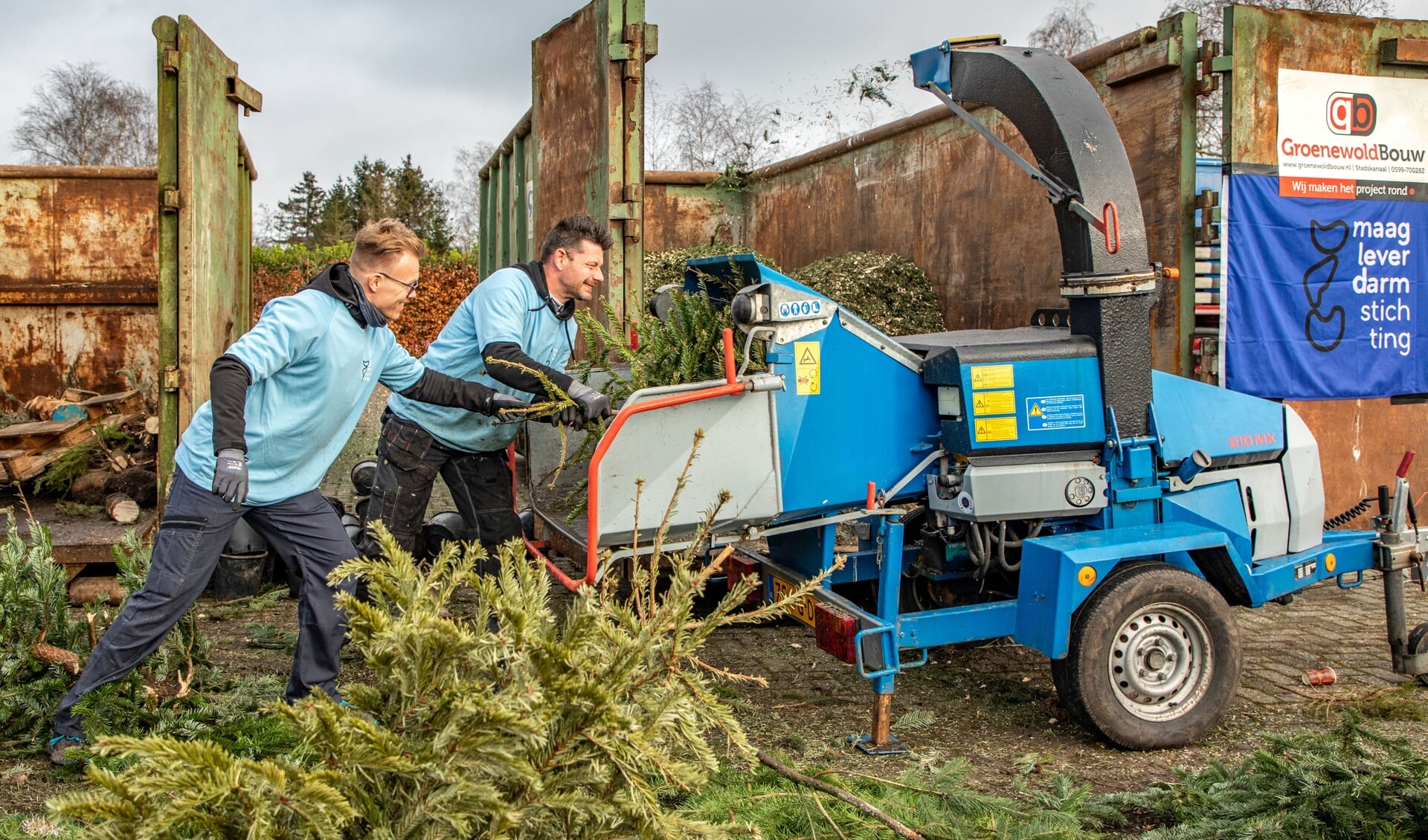 Rob Groenewold (links) en Chris Veltman zijn druk bezig met het versnipperen van de kerstbomen. 