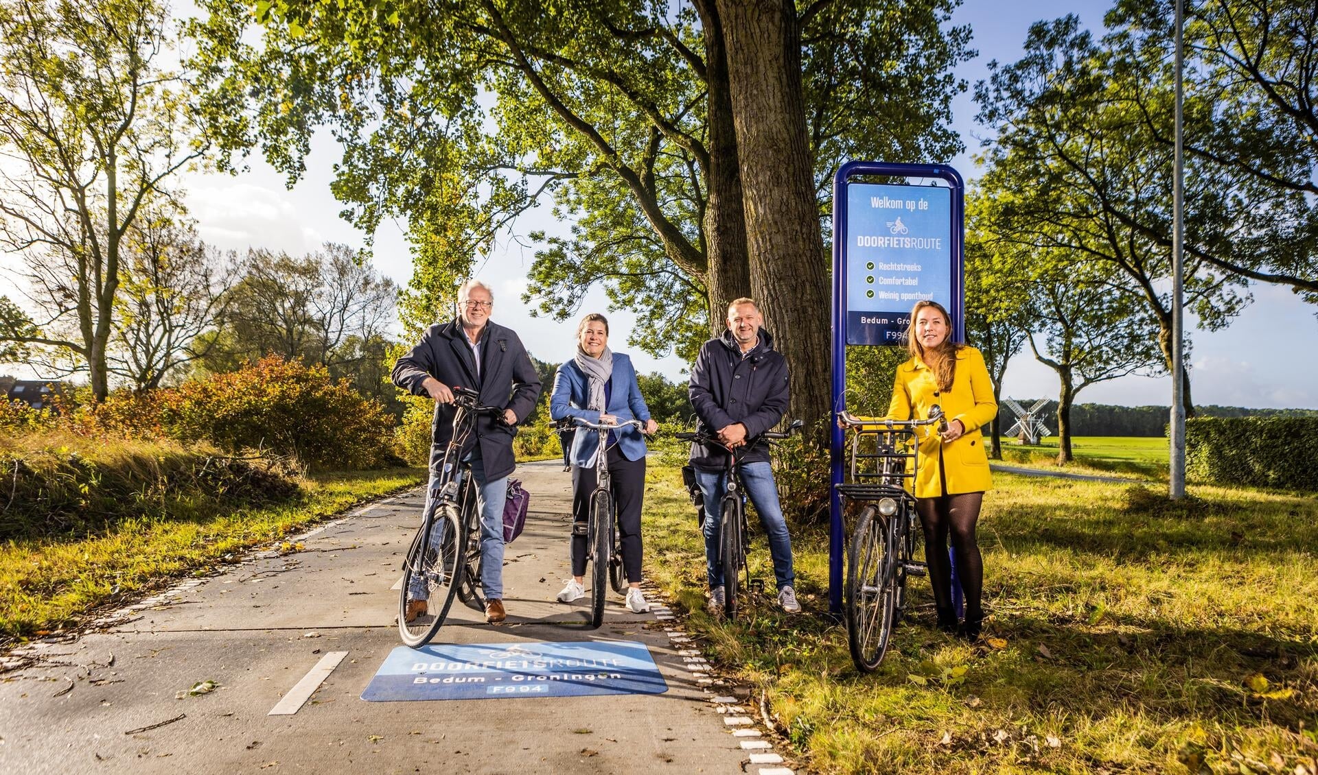 Philip Broeksma (wethouder gemeente Groningen), Fleur Gräper-Van Koolwijk (gedeputeerde provincie Groningen), Alex Wekema (wethouder gemeente Noordenveld) en Sandra Knoop (programmasecretaris Regio Groningen-Assen) poseren bij een bord en logo op de doorfietsroute Bedum-Groningen.