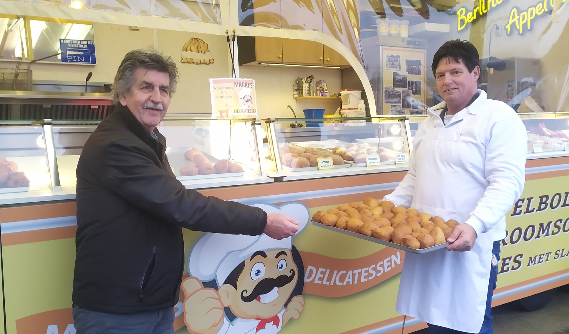 Mario Haisch overhandigt Frits Haan van de Voedselbank een schaal oliebollen.