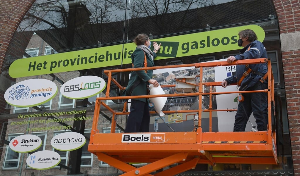 Gedeputeerde Fleur Gräper-van Koolwijk plakt de sticker 'het provinciehuis is nu gasloos' op een bouwbord.