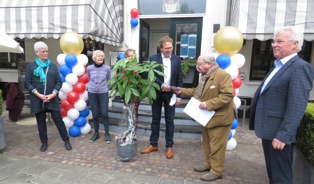 Maarten Rietveldt biedt, terwijl het bestuur van het Nut toekijkt, Frank Faber een grote plant plus een envelop aan.
