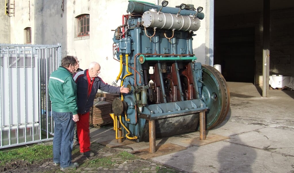 Een vrijwilliger van Siep&co legt een bezoeker de werking van een grote dieselmotor uit.