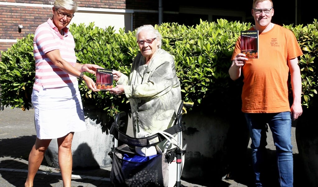 Marjan Dekens overhandigt een exemplaar van 'Woordtalenten' aan mevrouw Wildeveld-Tuizenga. Rechts Gerard Rozeboom, initiatiefnemer van 'Woordtalenten'.