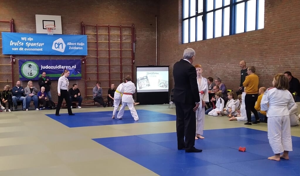 De deelnemers judoën onder toeziend oog van een scheidsrechter.