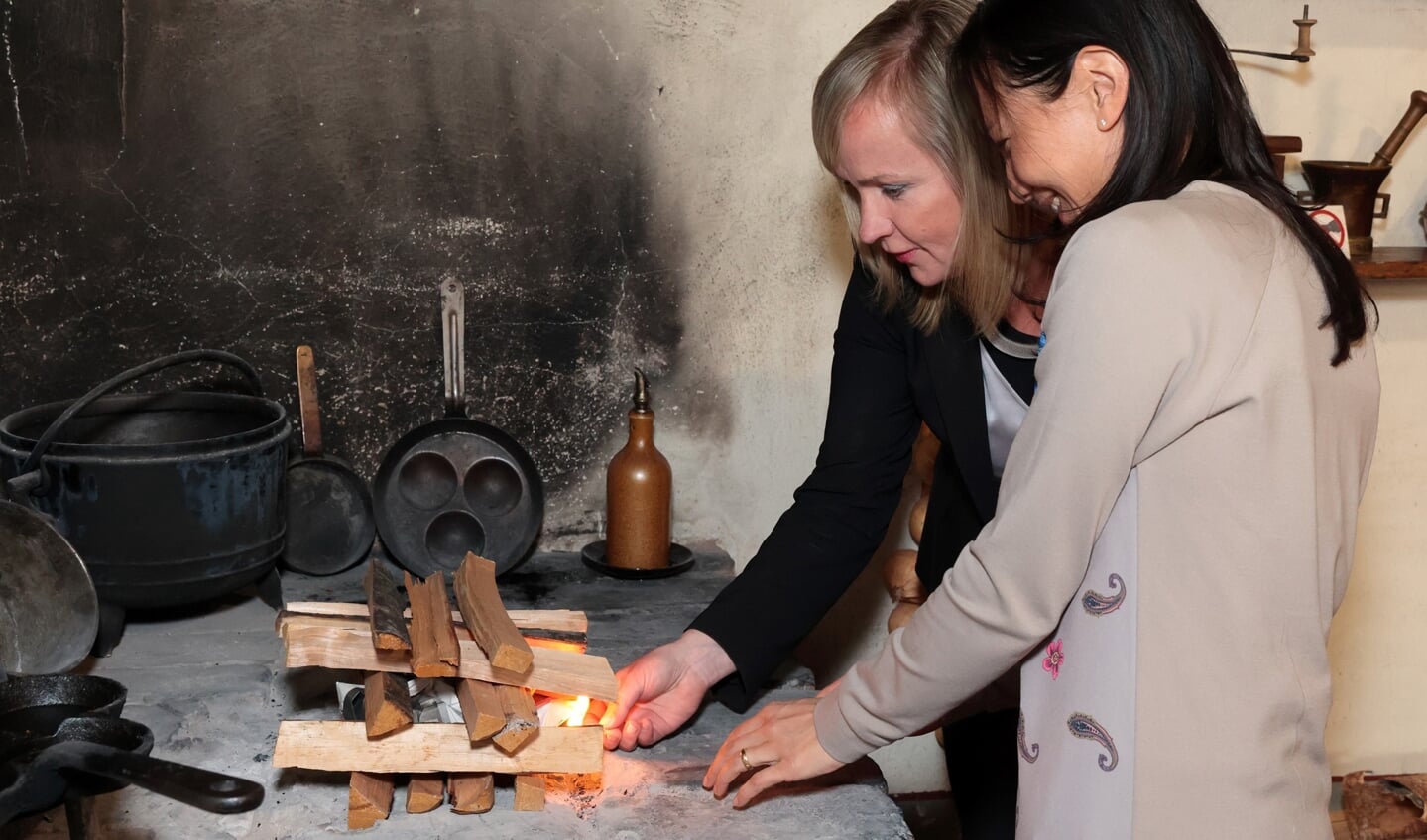De ambassadeurs Aiga Liepina (links) en  Claudia Pieterse openen   de expositie met het ontsteken van een vuurtje.
